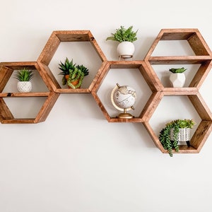 May include: A set of six hexagonal wooden shelves in a honeycomb pattern, mounted on a white wall. Each shelf is decorated with small potted plants and a globe.