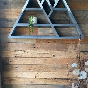 May include: Gray wooden mountain-shaped shelf with multiple shelves. The shelf is mounted on a wood wall.