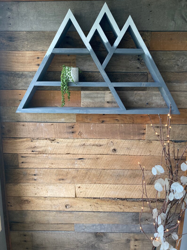 May include: Gray wooden mountain-shaped shelf with multiple shelves. The shelf is mounted on a wood wall.