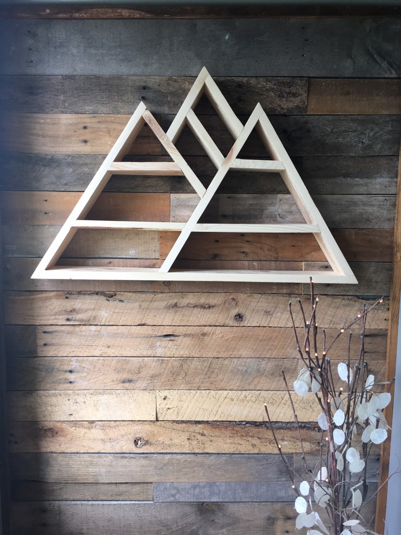 May include: A wooden shelf shaped like a mountain range with multiple shelves. The shelf is mounted on a rustic wood wall.