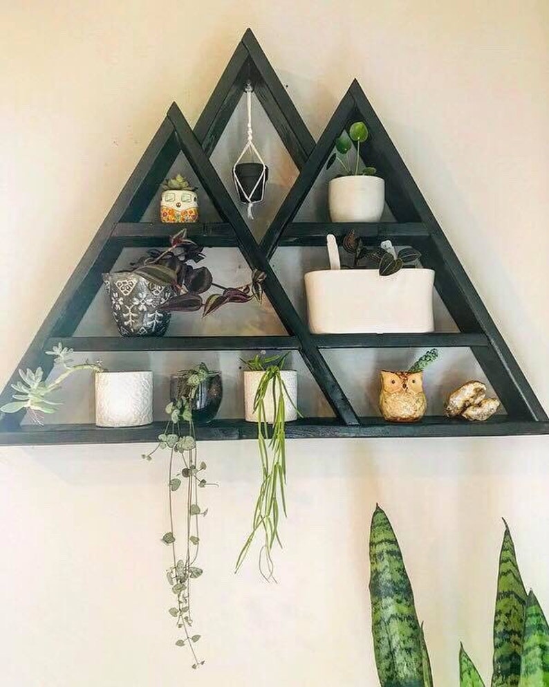 May include: A black wooden triangular shelf unit with multiple shelves, displaying various potted plants and a small owl figurine. The shelf is mounted on a white wall.