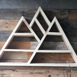 K&ouml;nnte beinhalten: Wandregal aus Holz in Form einer Bergkette mit mehreren dreieckigen Regalbrettern. Das Regal ist aus hellem Holz und hat einen rustikalen Look.