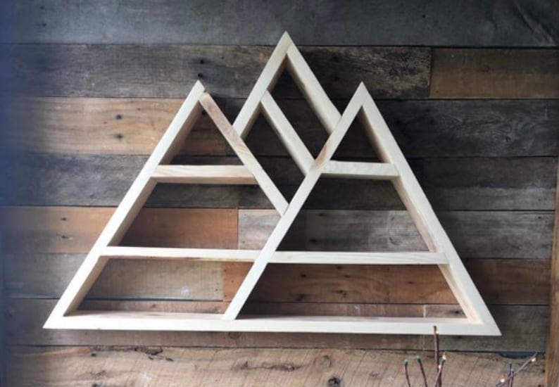 K&ouml;nnte beinhalten: Wandregal aus Holz in Form einer Bergkette mit mehreren dreieckigen Regalbrettern. Das Regal ist aus hellem Holz und hat einen rustikalen Look.