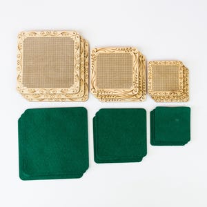 Pode incluir: Um conjunto de molduras de madeira para bordado em três tamanhos, com desenhos decorativos nos cantos. Abaixo das molduras, três pilhas de peças quadradas de feltro verde escuro, que oferecem contraste de cor e textura.
