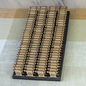 May include: A display of small, rectangular wooden tags with floral designs, arranged in rows on a black base. The tags are light brown with etched details, creating a textured appearance. The arrangement suggests a craft or organizational theme.