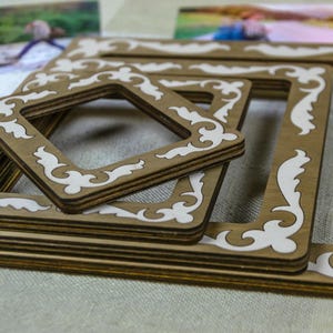 Könnte beinhalten: Eine Sammlung von Holzbilderrahmen in verschiedenen Größen, mit hellbraunem Finish und weißen dekorativen Akzenten. Die Rahmen sind gestapelt und angeordnet, wodurch ein geschichteter Effekt entsteht. Das Design umfasst verzierte, fließende Muster.