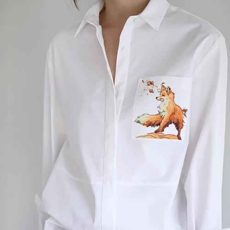 May include: White long-sleeve button-down shirt with a fox graphic on the pocket.