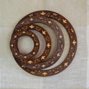May include: Four wooden rings with intricate floral designs, each ring is a different size and nested inside the other. The rings are brown with a light brown floral pattern.