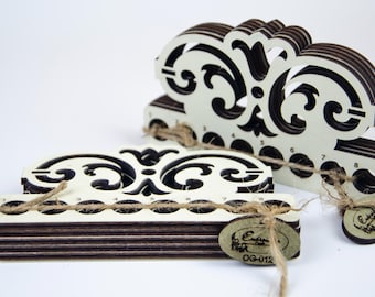 May include: Two laser-cut wooden embroidery floss organisers with a decorative scrollwork top and eight circular holes numbered one through eight. Each organiser is tied with natural twine and features an oval wooden tag labelled OG-012.