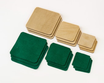 Op de afbeelding: Een assortiment vierkante onderzetters in verschillende maten. Sommige zijn gemaakt van lichtbruin hout met een rasterpatroon, andere van groen vilt. De onderzetters zijn in stapels op een wit oppervlak gerangschikt.