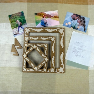 May include: Three nested rectangular wooden frames with white decorative scrollwork patterns, two small triangular wooden stands, three rectangular photographic prints, and a white fabric square featuring a line drawing of mushrooms.