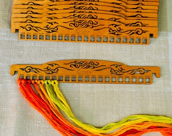 May include: Wooden embroidery floss organizers with a decorative design and numbered slots. Several organizers are stacked, with one displaying colorful threads in shades of orange and yellow. The word "Embroideries" is printed on the organizers.