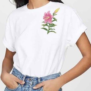 May include: A white t-shirt with a pink lily flower embroidered on the left chest.