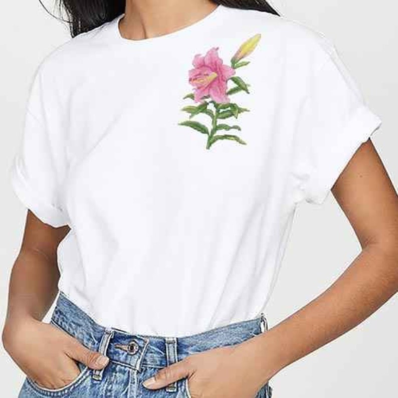 May include: A white t-shirt with a pink lily flower embroidered on the left chest.