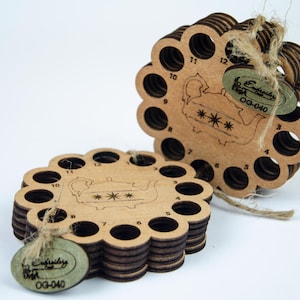 Może przedstawiać: Dwa drewniane organizery na nici z falistą krawędzią i ponumerowanymi otworami. Każdy organizer ma laserowo wytrawiony wzór czajnika i małą etykietę z tekstem. Organizery są związane sznurkiem.