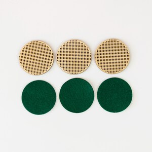 May include: Six round coasters. Three are made of light-colored wood with a perforated design. The other three are dark green felt. The coasters are arranged in two rows of three on a white background.