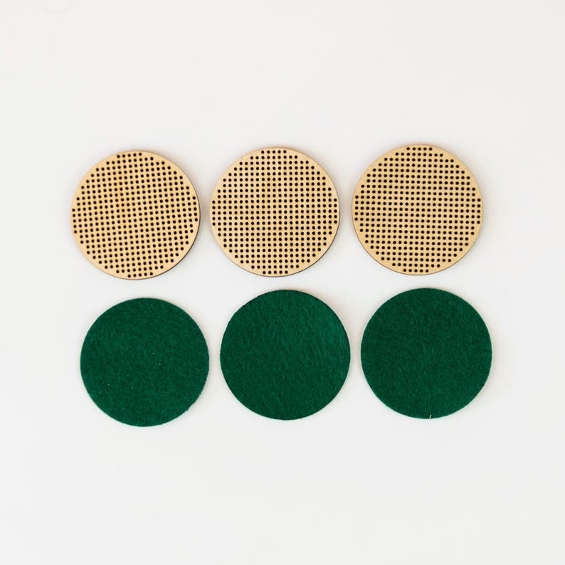 May include: Six round coasters. Three are made of light-colored wood with a perforated design. The other three are dark green felt. The coasters are arranged in two rows of three on a white background.