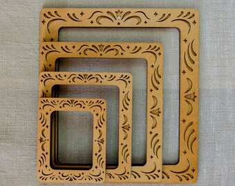 May include: A set of four nested rectangular frames made of light brown wood. Each frame features a consistent laser-cut border pattern consisting of symmetrical swirls, curved lines, and small four-pointed star shapes along the entire perimeter.
