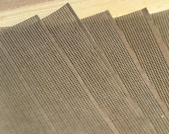 May include: A stack of rectangular brown baking mats featuring a fine, uniform mesh grid pattern. Each mat has a smooth, solid border along the edges, and the sheets are layered in a fanned arrangement to show the textured surface.