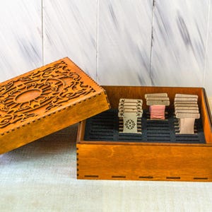 May include: A wooden box with a decorative carved lid, open to show compartments with thread spools. The box is stained a warm brown, and the lid has an intricate design. The thread spools are in various colours.
