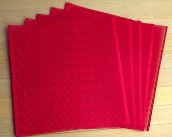 May include: A set of five square red plastic mesh sheets arranged in a fanned stack. Each sheet features a uniform grid pattern with small, evenly spaced holes throughout the surface, providing a semi-transparent appearance across the stack.