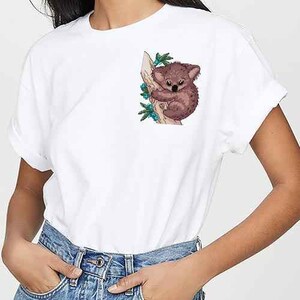 May include: White t-shirt with a graphic of a koala bear sitting on a tree branch with green leaves.