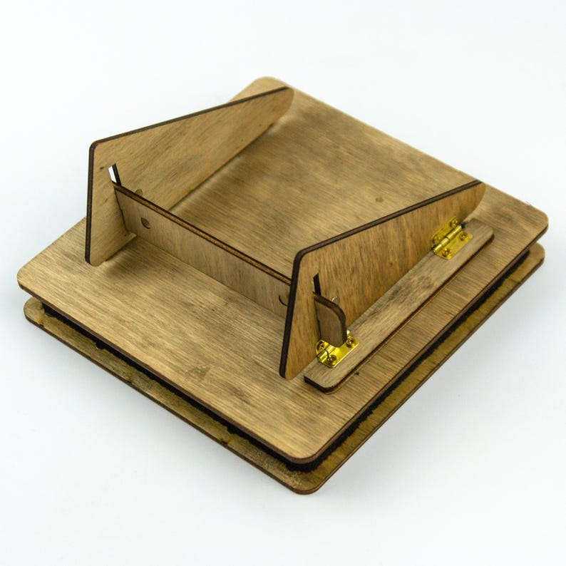 Op de afbeelding: Een houten ezel met een opvouwbare standaard en twee gouden scharnieren. De ezel is gemaakt van lichtbruin hout en heeft een natuurlijke afwerking.