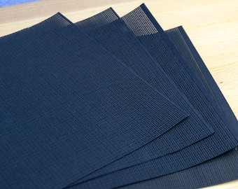 May include: A set of four rectangular dark navy blue placemats featuring a fine, uniform grid-like mesh texture. The placemats are layered in a slightly fanned arrangement, showcasing the consistent woven pattern and the deep blue colour throughout.
