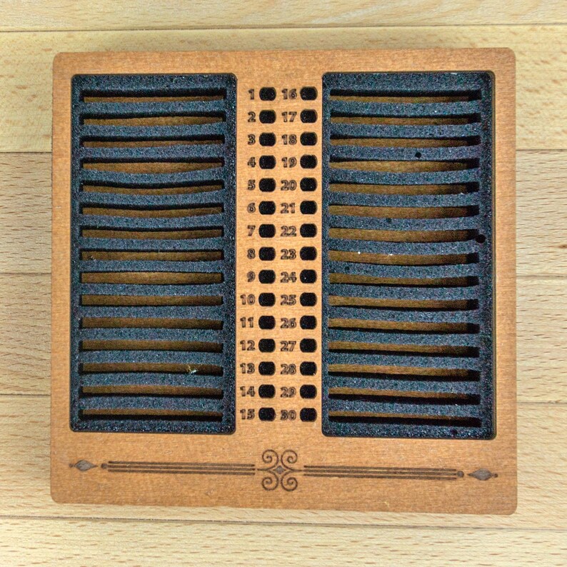 May include: A wooden calendar with 30 numbered slots, each separated by black foam. The numbers 1-30 are listed on the right and left sides. The calendar has a decorative design at the bottom.