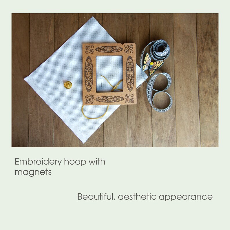 May include: A wooden embroidery hoop with a decorative design and magnets. The hoop is on a white fabric with a gold thread and a thimble. A measuring tape with a butterfly design is on a wooden surface.