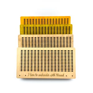 May include: Four wooden thread organizers in shades of yellow and beige, each with rows of numbered holes for embroidery thread. The bottom organizer has the text "I love to embroider with thread."