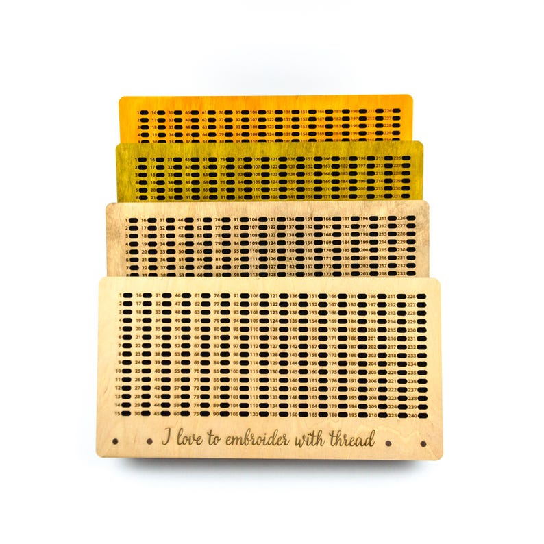 May include: Four wooden thread organizers in shades of yellow and beige, each with rows of numbered holes for embroidery thread. The bottom organizer has the text "I love to embroider with thread."