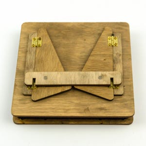 Op de afbeelding: Een houten opvouwbare standaard met messing scharnieren. De standaard is gesloten en plat gevouwen.