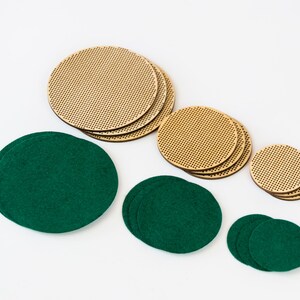 May include: An assortment of round coasters in two materials: light brown, perforated wood and dark green felt. The coasters are in various sizes, arranged on a white background. The wooden coasters have a grid-like pattern.