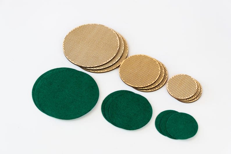 May include: An assortment of round coasters in two materials: light brown, perforated wood and dark green felt. The coasters are in various sizes, arranged on a white background. The wooden coasters have a grid-like pattern.