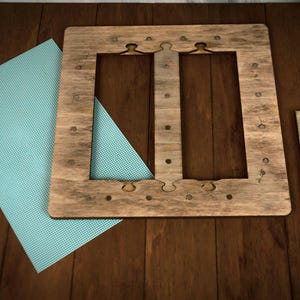 May include: A wooden frame with decorative cutouts and a separate wooden piece, alongside a light blue sheet with a dotted pattern. The frame has small metal accents. The items are arranged on a dark wooden surface.