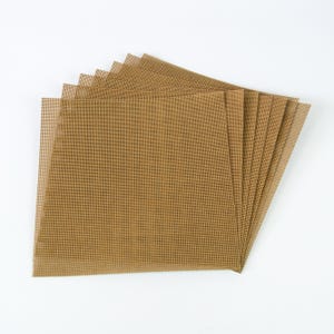Könnte beinhalten: Ein Stapel brauner, quadratischer, gitterartiger Blätter, die vor einem weißen Hintergrund aufgefächert sind. Die Blätter haben ein Rastermuster und scheinen aus einem gewebten Material zu bestehen. Die Farbe ist ein warmer, erdiger Ton.