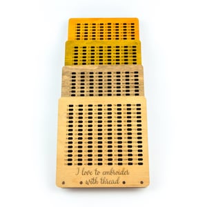 Op de afbeelding: Een houten borduurring met een raster van genummerde gaten. De ring is gemaakt van licht hout en heeft een natuurlijke afwerking. De tekst "Ik hou van borduren met draad" is gegraveerd op de onderkant van de ring.