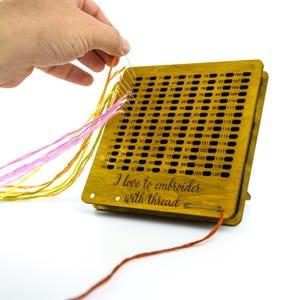 May include: A wooden thread organiser with a grid of numbered holes for storing embroidery floss. The organiser has a stand and the text "I love to embroider with thread" is engraved on the front.