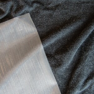 May include: A close-up of a gray fabric with a white mesh fabric overlay. The mesh fabric has a grid pattern.