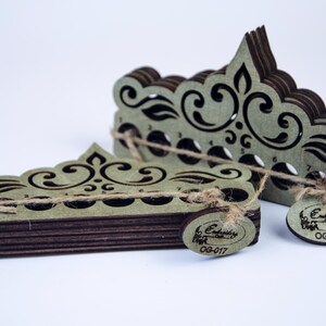 Könnte beinhalten: Zwei Holz-Stickgarn-Organizer in einem geschichteten Design. Die Organizer sind olivgrün mit dunkelbraunen Kanten und verfügen über dekorative Ausschnitte. Jeder Organizer hat ein kleines Etikett mit Text und ist mit Bindfaden gebunden.