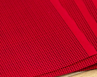 May include: A bright red fabric featuring a dense, uniform pattern of small, evenly spaced black dots. The material has a distinct grid-like texture created by the perforated design, with a smooth, solid red border visible along the right edge.