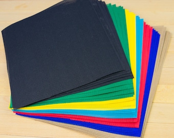 May include: A stack of square plastic mesh sheets arranged in a fan pattern. The sheets feature a grid of small holes and come in a variety of colours including black, green, yellow, light blue, red, dark blue, and tan, layered to show each colour.