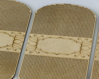 Op de afbeelding: Close-up van verschillende onafgewerkte houten ambachtelijke stukken. Elk stuk heeft een geperforeerd bovendeel en een decoratief, gegraveerd ontwerp met een ovale midden. De stukken zijn lichtbruin.