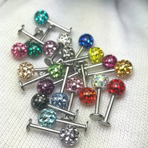 Op de afbeelding: Een verzameling kleurrijke, met edelstenen bezette lipringen, elk met een andere gekleurde edelsteen. De ringen zijn gemaakt van roestvrij staal en hebben een kleine, ronde edelsteen in het midden. De edelstenen zijn in alle kleuren, waaronder rood, blauw, groen, geel en paars.