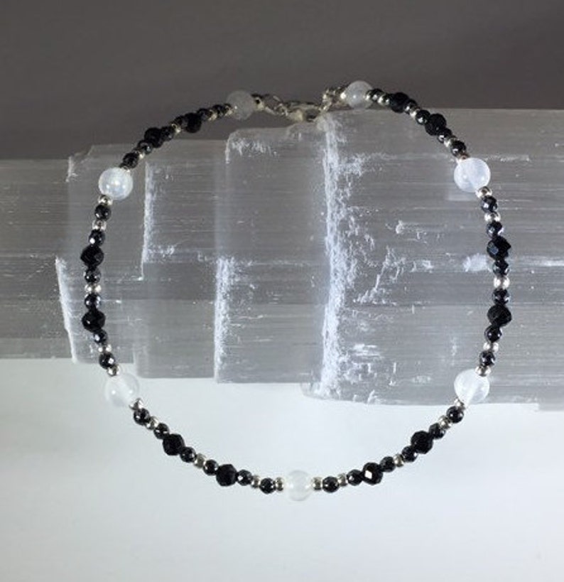May include: A black and white beaded bracelet with silver accents. The bracelet is made with small round beads and features a mix of black and white stones.