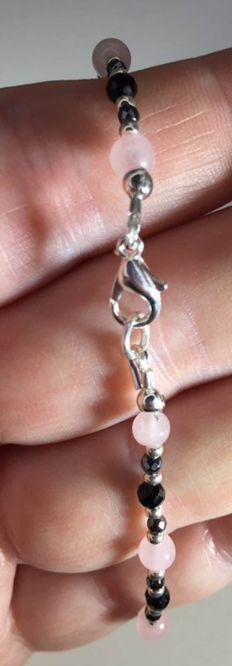 May include: A silver bracelet with alternating pink and black beads. The bracelet has a silver clasp.