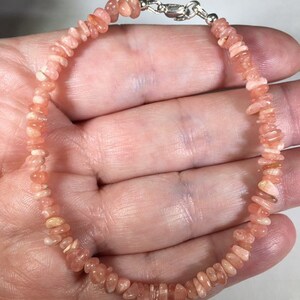 May include: A delicate bracelet featuring small, irregularly shaped, peach-colored gemstones. The stones are strung together, forming a continuous loop, and secured with a silver-colored clasp. The bracelet is designed to be worn around the wrist.