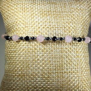May include: A delicate bracelet with alternating black and pink beads. The bracelet is made with small, round beads and is strung on a silver chain.