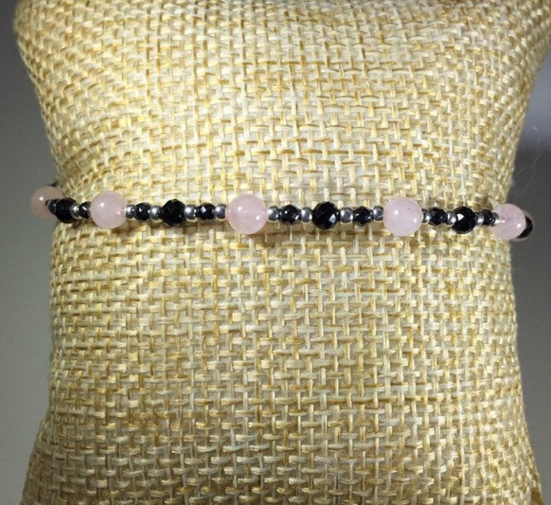 May include: A delicate bracelet with alternating black and pink beads. The bracelet is made with small, round beads and is strung on a silver chain.